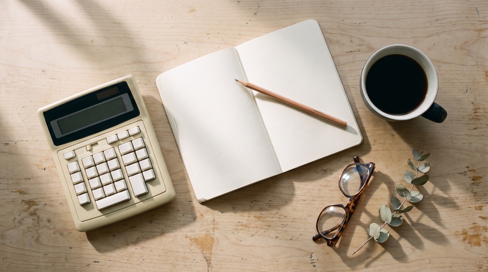 A calculator, notebook and coffee on a warm table