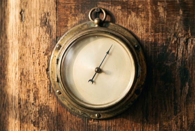 A brass barometer with a blank face on a wooden wall