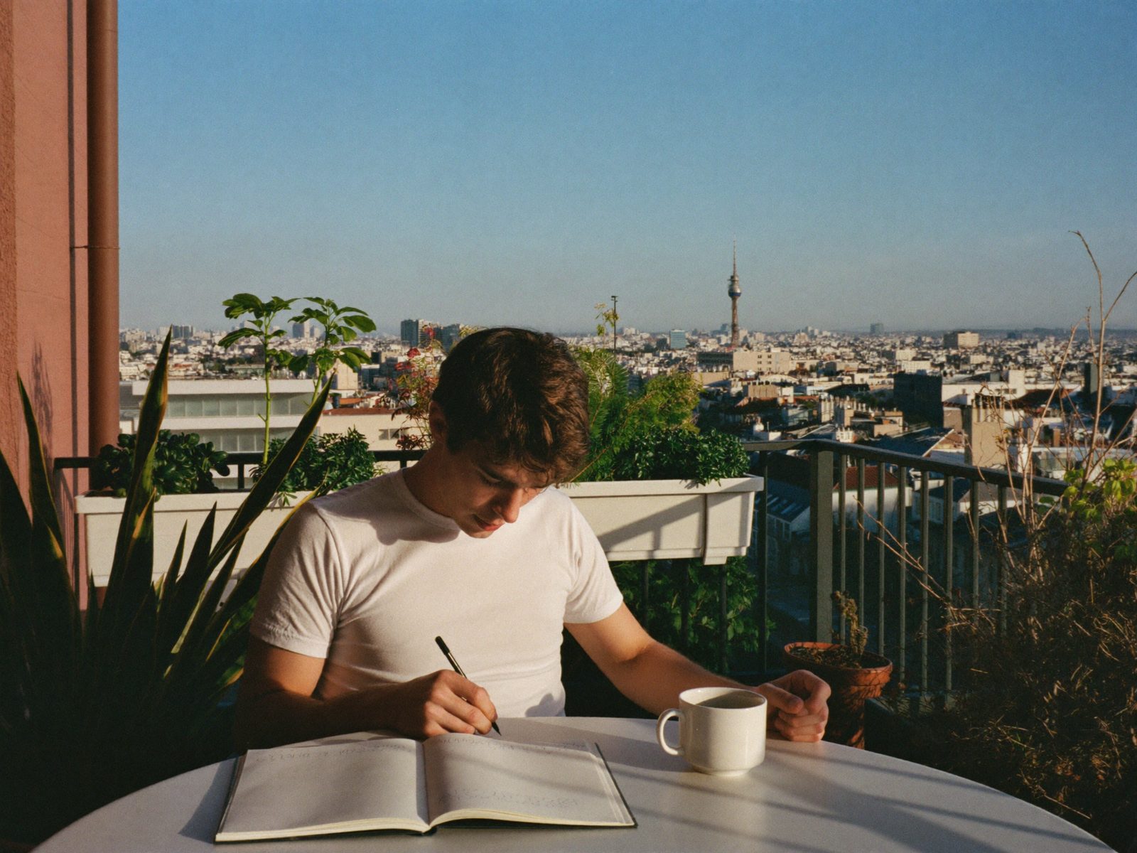 Writing in a journal on a plant-filled balcony at sunrise
