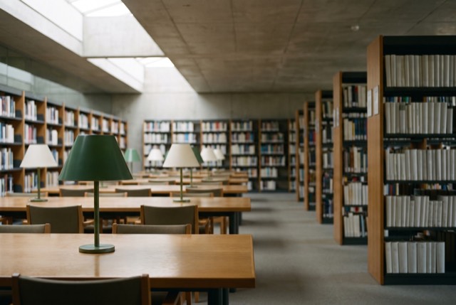 A sunlit library reading room with green lamps