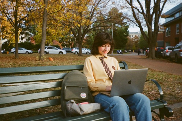 A student on a campus bench under autumn trees