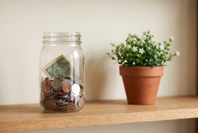 A jar filling with coins beside a plant