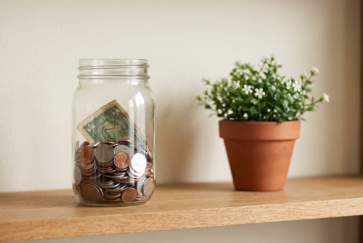 A jar filling with coins beside a plant